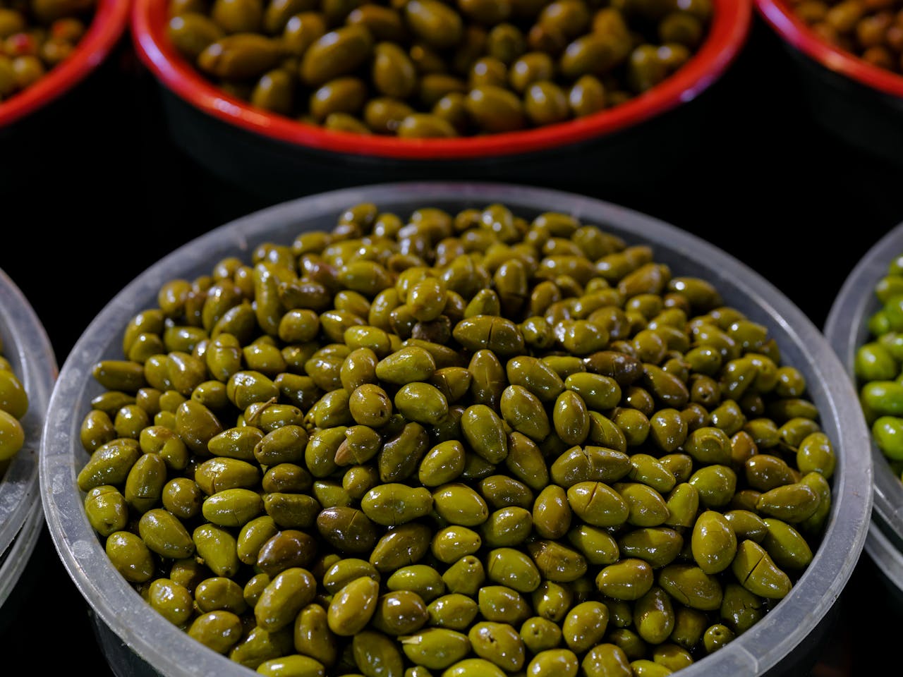 A close-up view of fresh green olives displayed in bowls at a market, highlighting their vibrant color and texture.